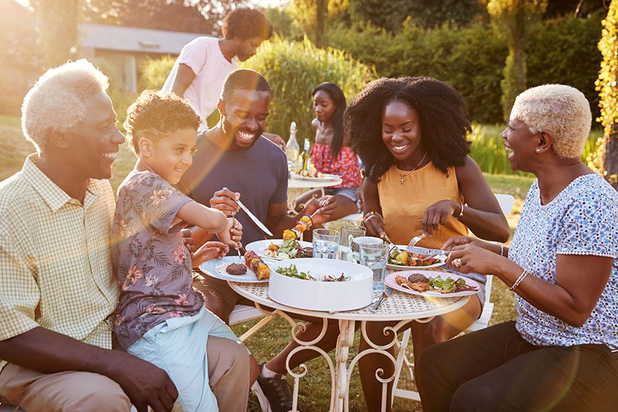 About Our Agency - Multi-Generation Family Eating Outdoors at a Table in the Garden at Sunset